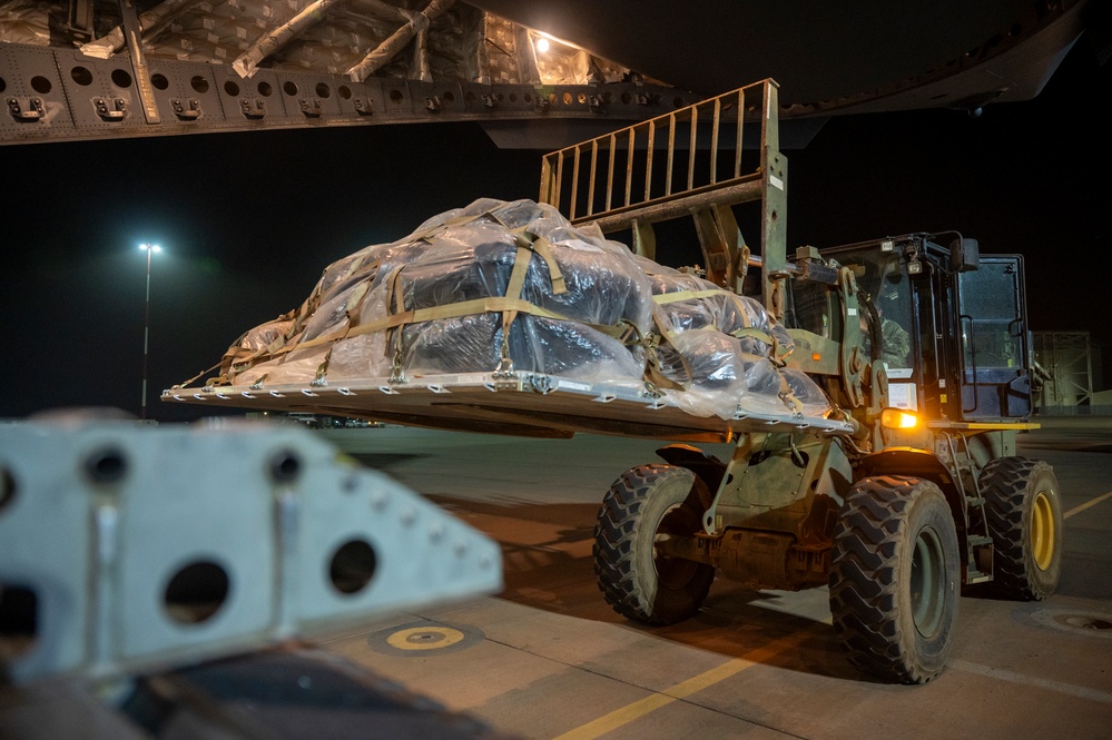 Military personnel using forklift to load palletized equipment onto C-17 aircraft