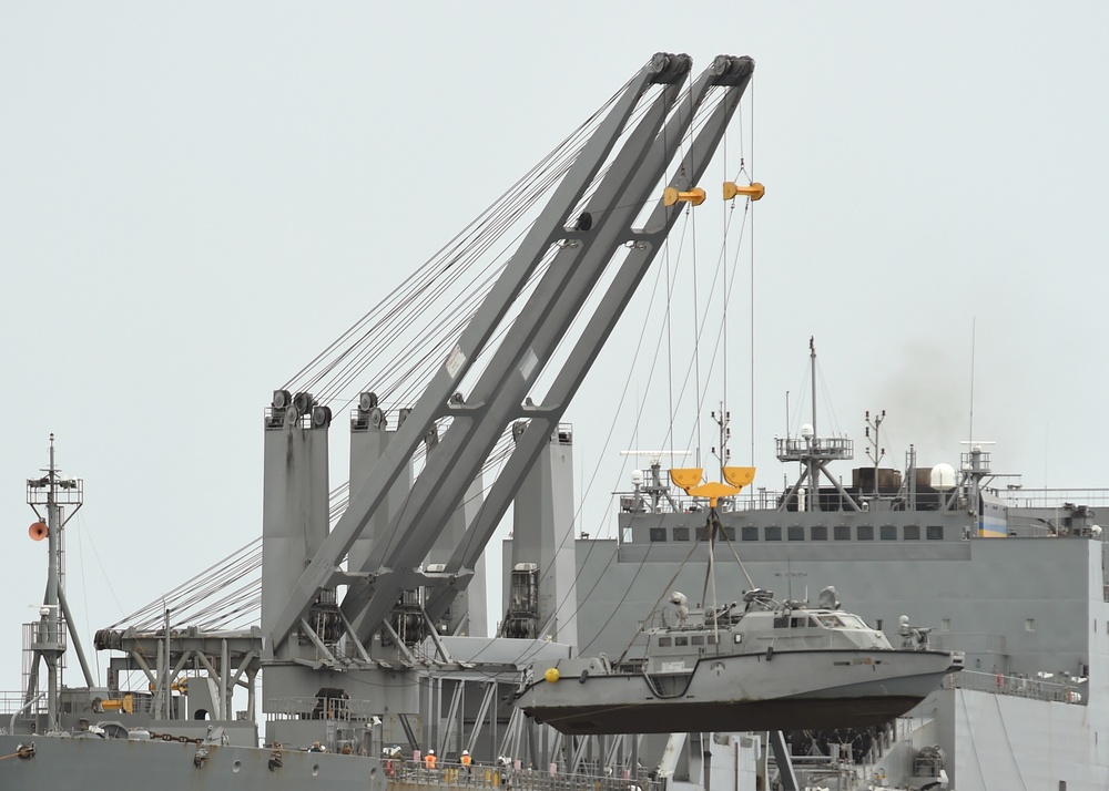 Navy expeditionary logistics personnel operating crane to load equipment onto military sealift ship