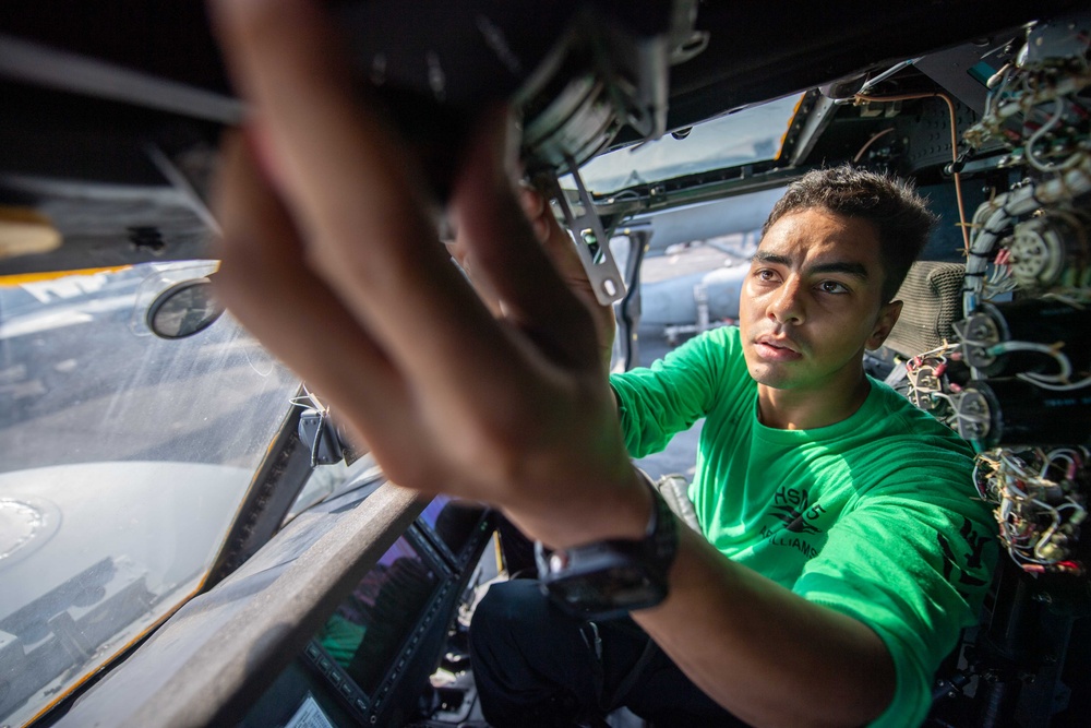 Aviation electrician performing maintenance on a helicopter aboard a carrier
