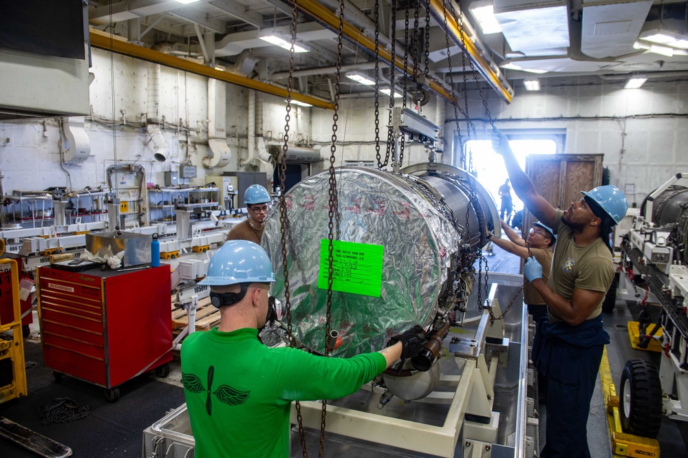 Sailors moving a jet engine in the jet shop aboard an aircraft carrier