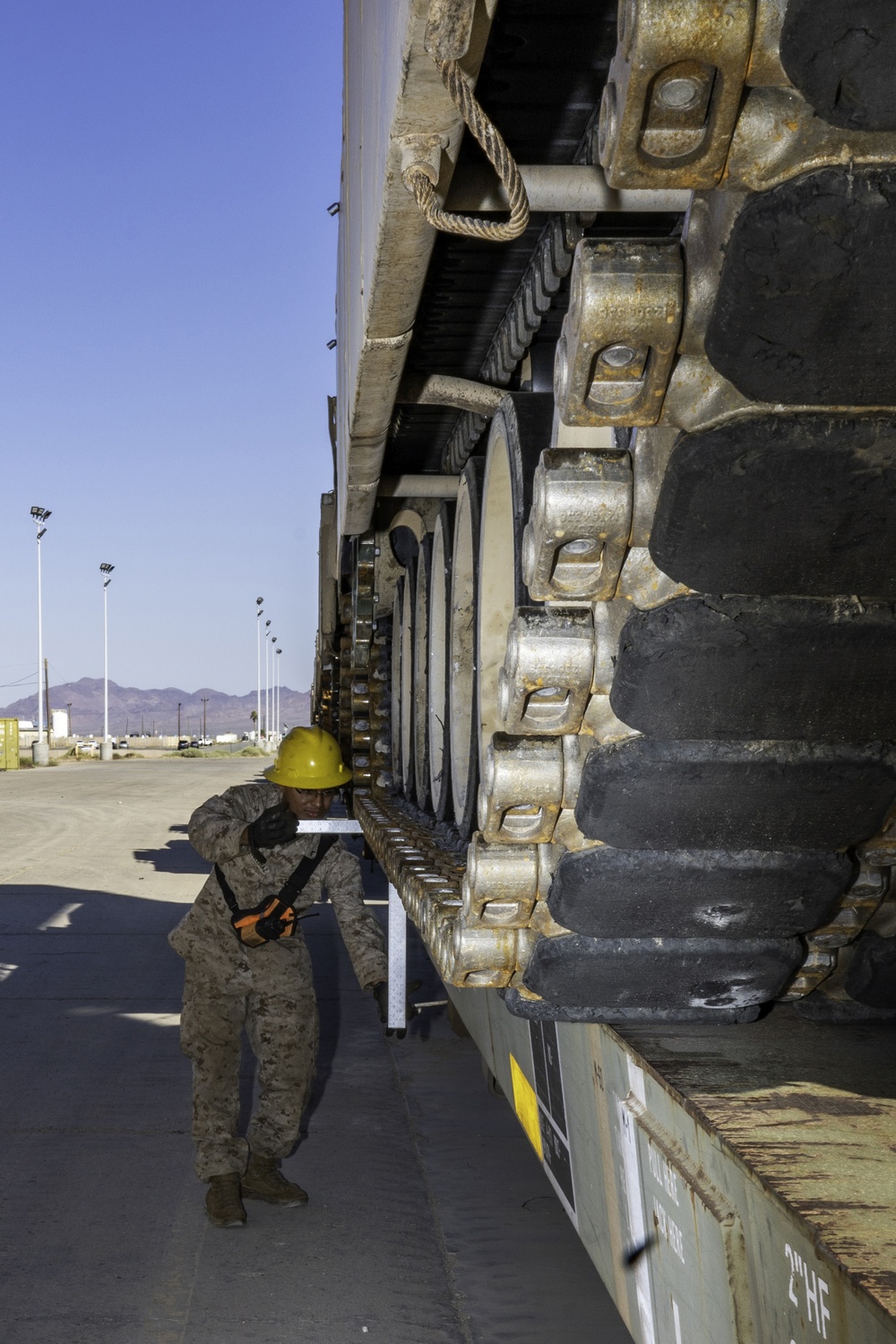 A Marine measures tracks on an M1A1 Abrams tank being loaded onto rail cars for transport